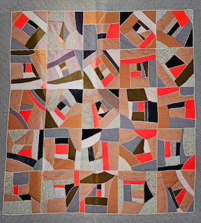 Crazy quilt with colorful geometric patchwork in red, orange, tan, gray and black fabrics