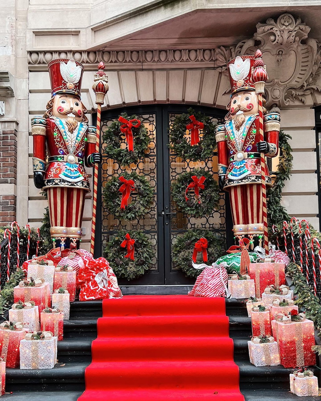 Two large nutcracker soldier statues flank decorated entrance with Christmas wreaths, gifts, and red carpet