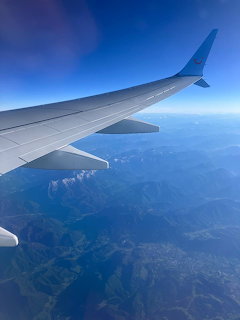 Airplane wing seen from a window above a blue sky and distant mountains