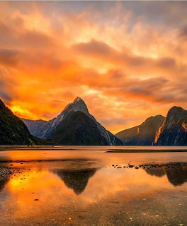 Sunset over Milford Sound with mountain peaks reflected in calm water