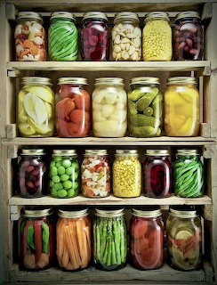 Four wooden shelves displaying rows of glass mason jars filled with colorful pickled and preserved vegetables