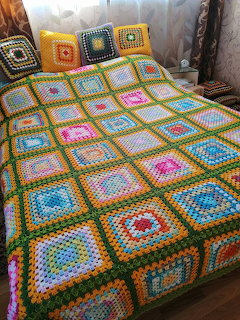 Bed with a colorful crocheted granny square blanket and matching pillows