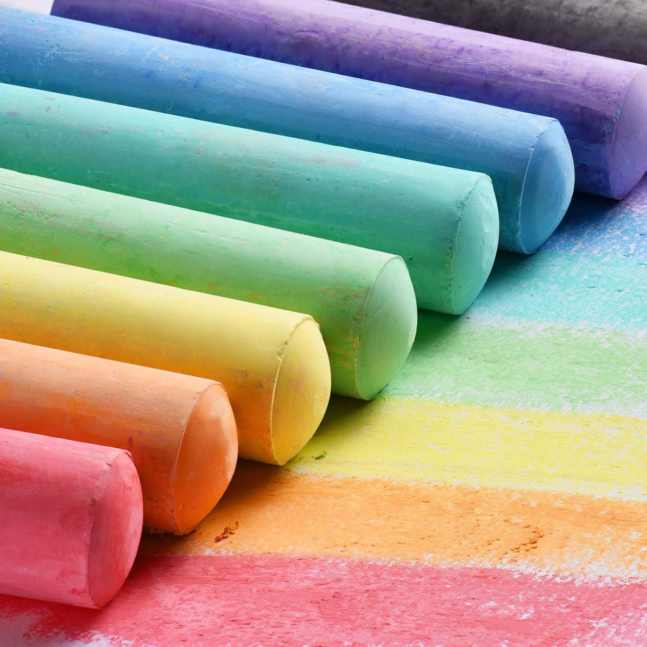 Rainbow colored chalk sticks lined up diagonally with colorful chalk dust marks on paper