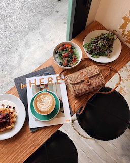 Overhead cafe table with coffee, pastries, berries, magazine and woven bag on wooden surface