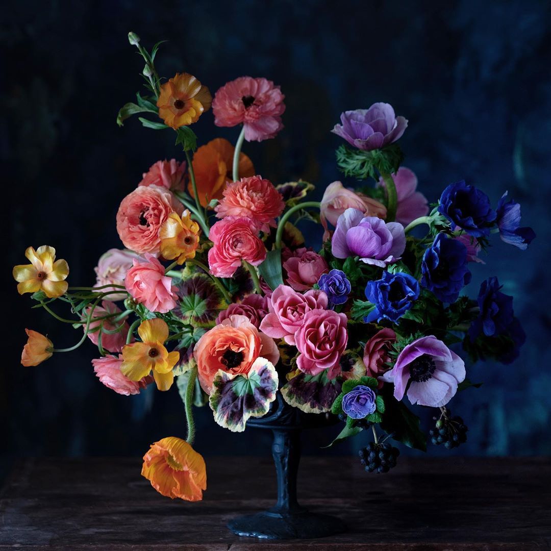 Colorful flower bouquet with pink, purple, orange, and yellow blooms in vase against dark background