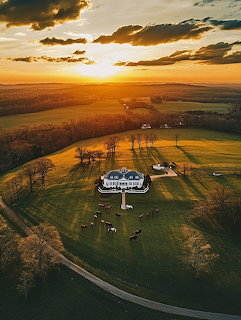 Aerial view of white farmhouse in fields at sunset with golden light and dramatic clouds