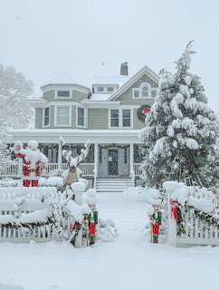 Snow-covered Victorian house decorated for Christmas with Santa figures and garland on white picket fence