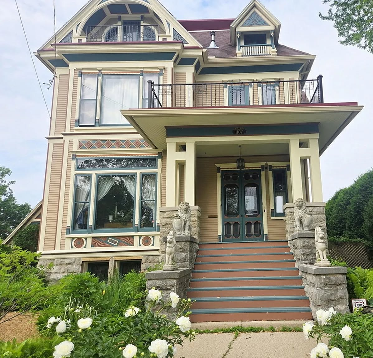Victorian-style house with front porch, steps, stone lion statues, and white flowers