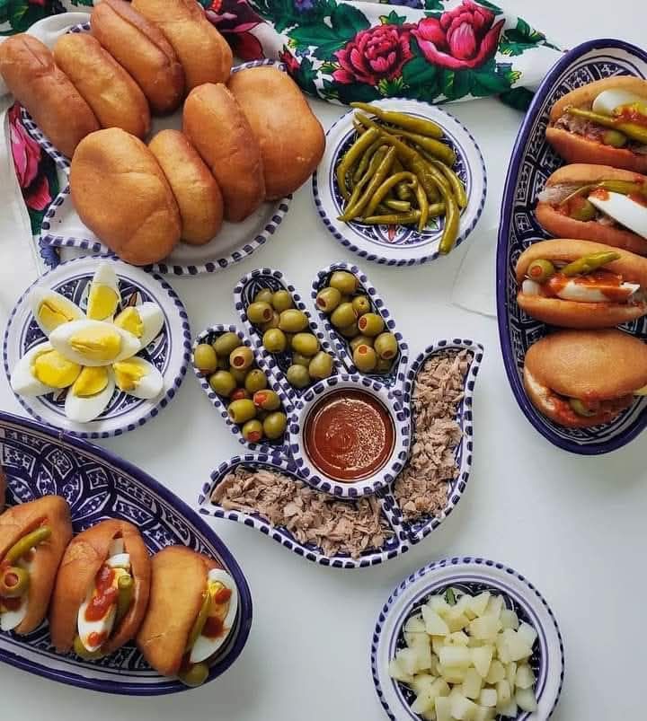 Overhead view of golden fried Tunisian frykasy pastries on decorative plates with colorful garnishes and dipping sauce