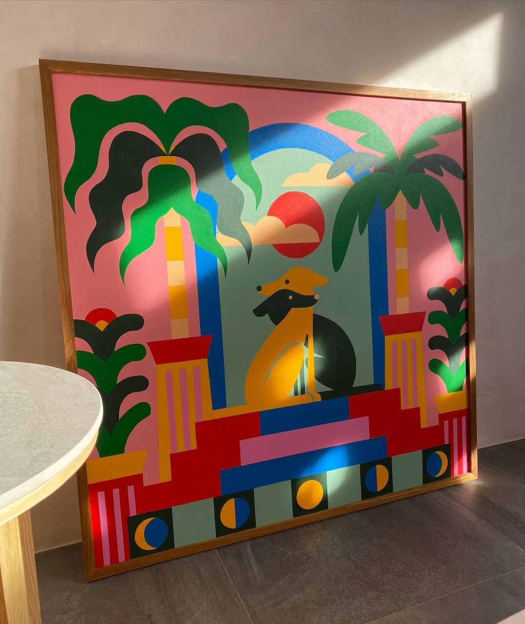 Framed colorful illustration with arches, palm trees, and a dolphin leaning against a wall indoors
