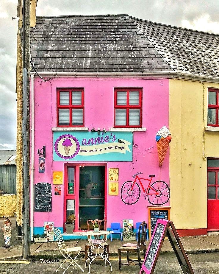 Bright pink ice cream shop with yellow side wall, bicycle and outdoor table on Irish street corner