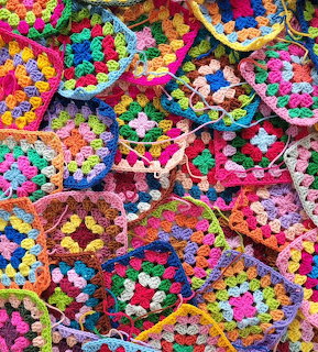 Pile of colorful crochet granny squares with rainbow yarn patterns in hexagonal shapes