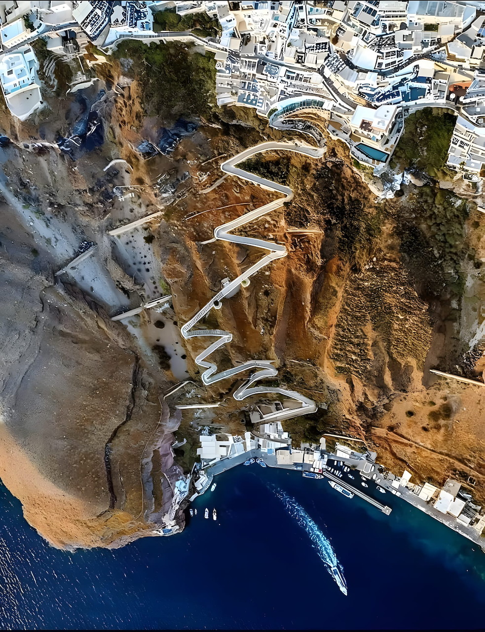 Aerial view of winding stone steps and white buildings on Santorini cliff leading down to blue water