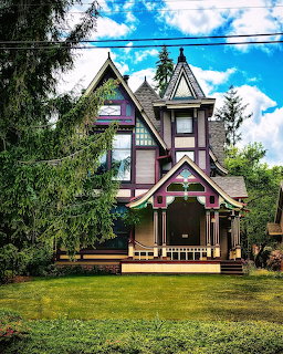 Pink Victorian house with ornate gables and trim on green lawn under blue sky