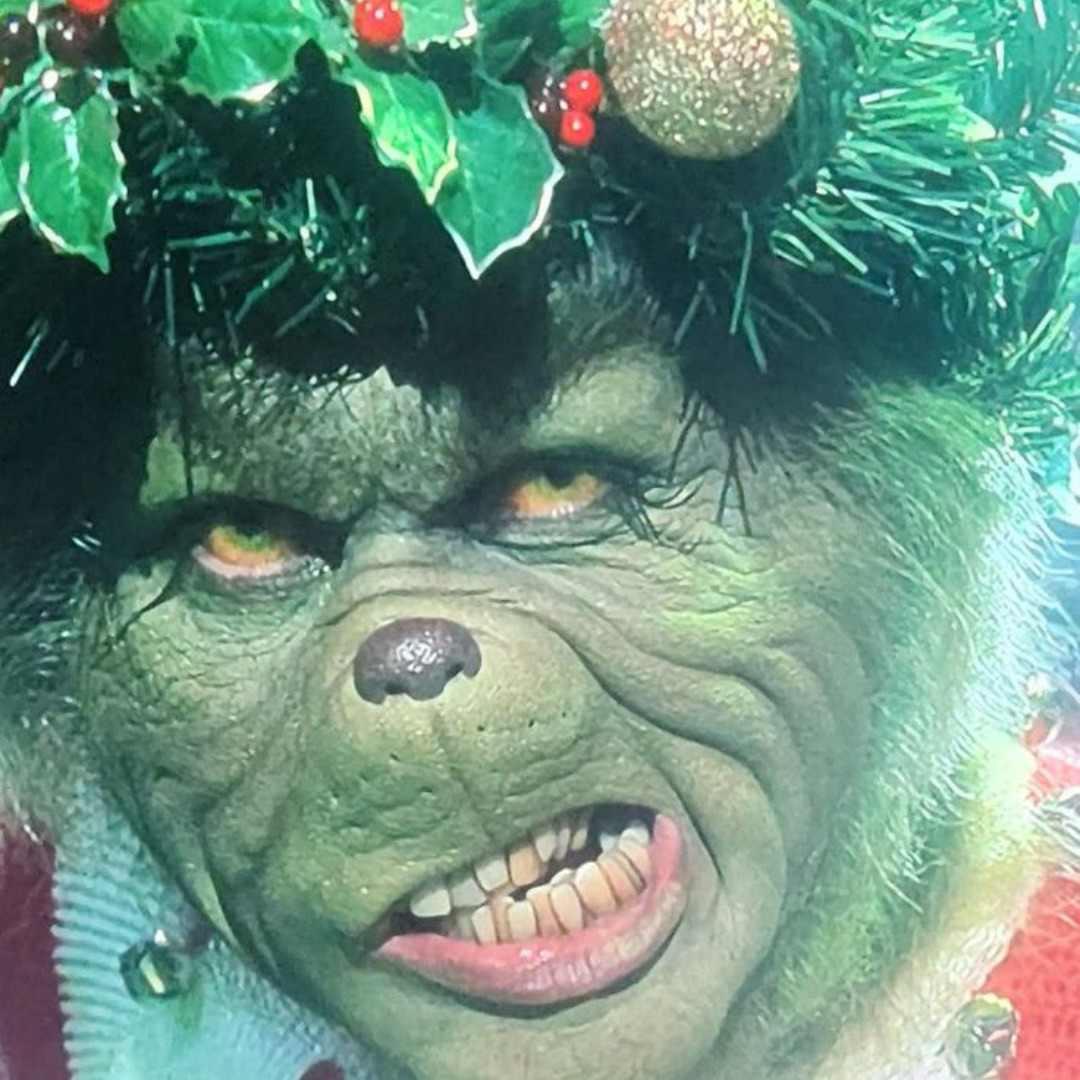 Close-up of the Grinch snarling with Christmas garland and holly around his head