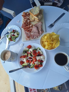 Overhead view of Mediterranean lunch with meats, salad, chips and coffee on white table