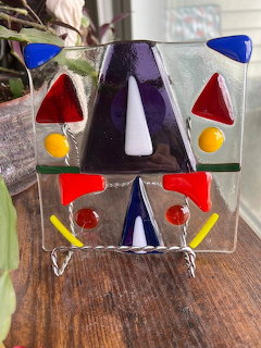 Colorful geometric fused glass suncatcher with triangles and circles on clear glass displayed on wooden surface
