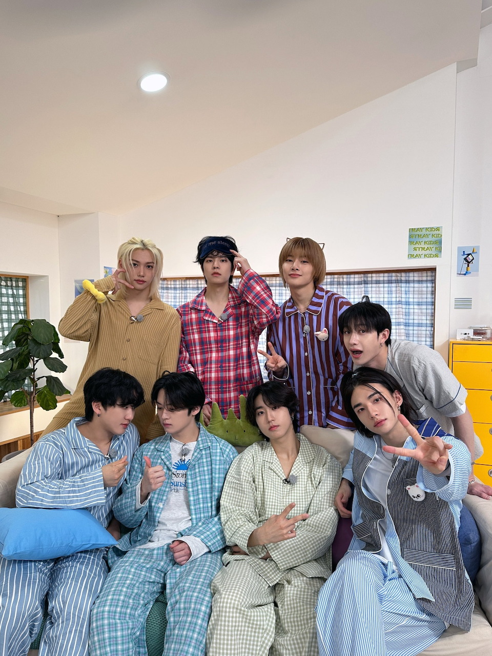 Eight young men in colorful pajamas posing together indoors, smiling and making peace signs