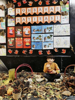 Child sitting with autumn leaves and pinecones in front of a kindergarten bulletin board with fall artwork