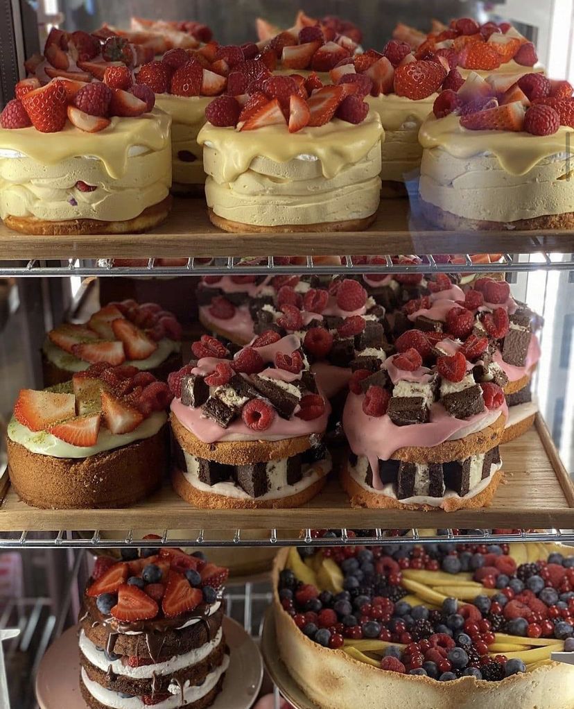 Bakery display shelf with multiple cakes decorated with fresh berries and cream