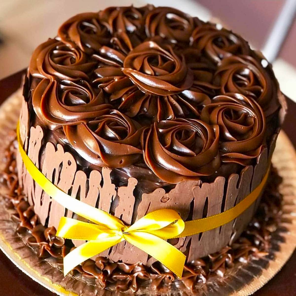 Round chocolate cake with rosette frosting, chocolate shard sides, and yellow ribbon