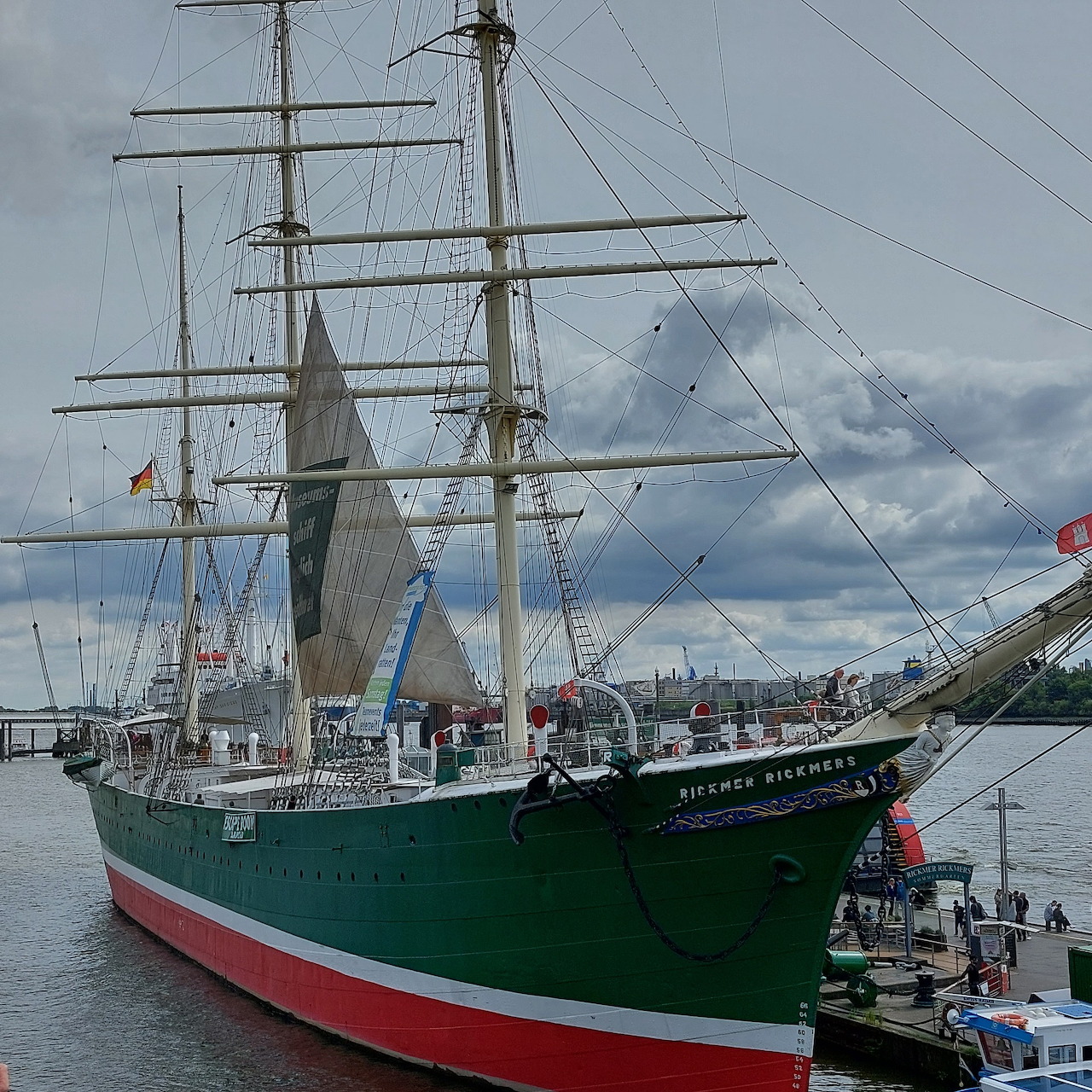 Green and white tall sailing ship moored at Hamburg harbor under cloudy sky