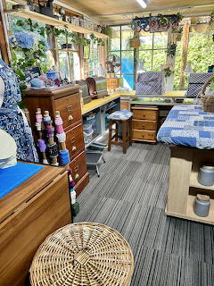 Interior of a cozy garden room with wooden drawers, craft supplies, plants, and a blue quilted daybed