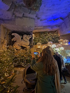 Woman at a Christmas market inside a cave with lit trees, lanterns, and a dragon wall carving