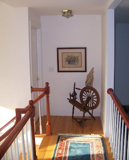 Wooden spinning wheel on a home staircase landing with wooden railings and framed artwork