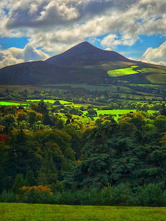 Great Sugar Loaf mountain rising above green fields and dense trees under dramatic cloudy sky