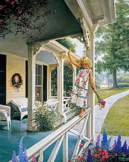 Girl in floral dress leaning over white porch railing reaching toward colorful flowers in garden