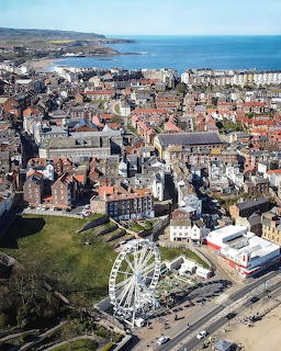 Aerial photograph of a coastal town with a Ferris wheel, dense buildings, and ocean view