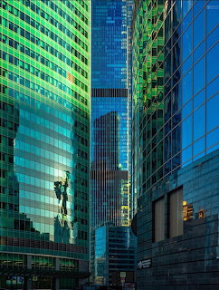 Upward view of tall modern glass skyscrapers in blue and green with reflective facades creating an urban canyon