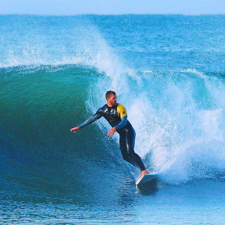 Surfer in a wetsuit riding a blue ocean wave with white spray