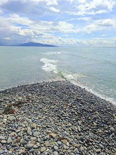 Pebble beach with turquoise ocean waves and cloudy sky over distant mountains