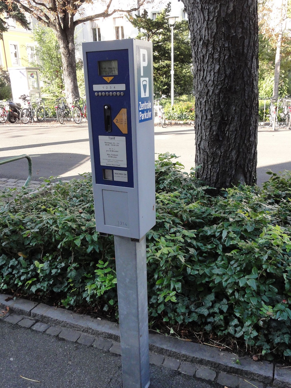 German parking pay station on a pole surrounded by green bushes on a city street
