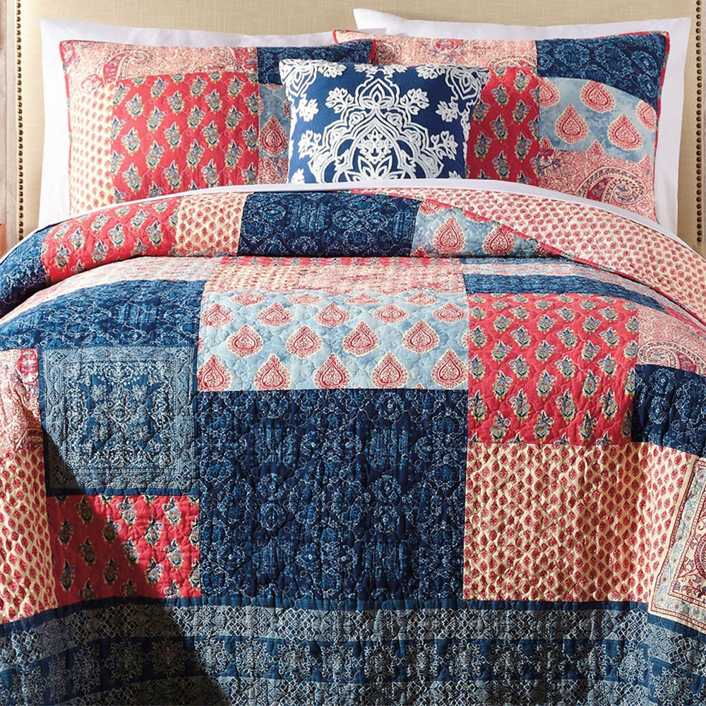 Patchwork quilt in coral, navy, and beige with matching pillows on white bed