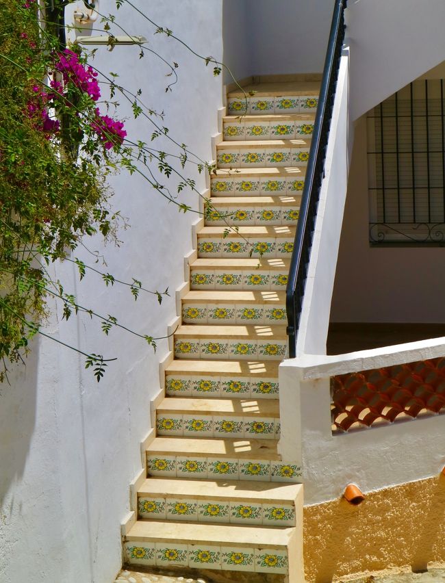 White staircase with colorful ceramic tiles, pink bougainvillea, and vines in a Mediterranean setting