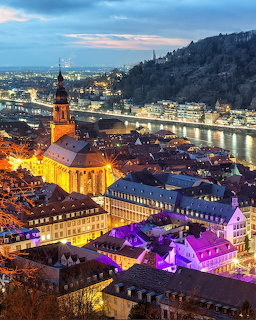 Heidelberg old town at dusk with illuminated buildings, castle on hill, and Neckar River reflecting city lights