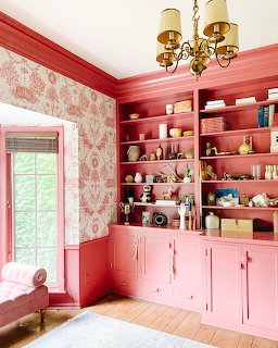 Pink painted room with built-in shelves, floral wallpaper, brass chandelier, and decorative objects