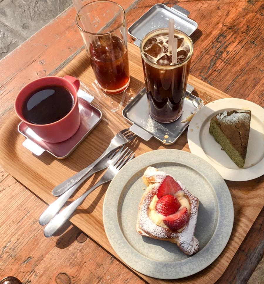 Wooden tray with hot black coffee, iced americano, strawberry danish, and green tea cake slice