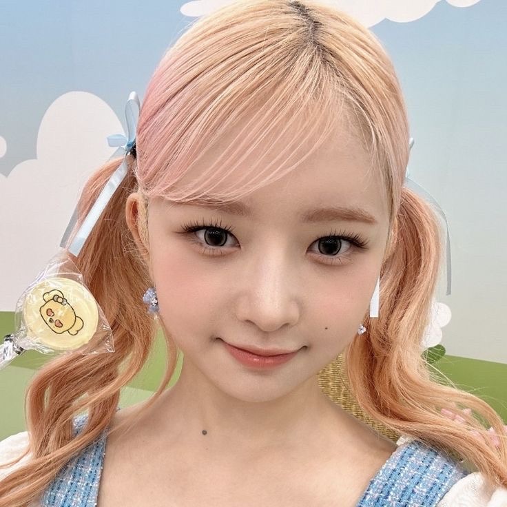Close-up portrait of a young woman with pink twin-tail hair and a blue top against a pastel background