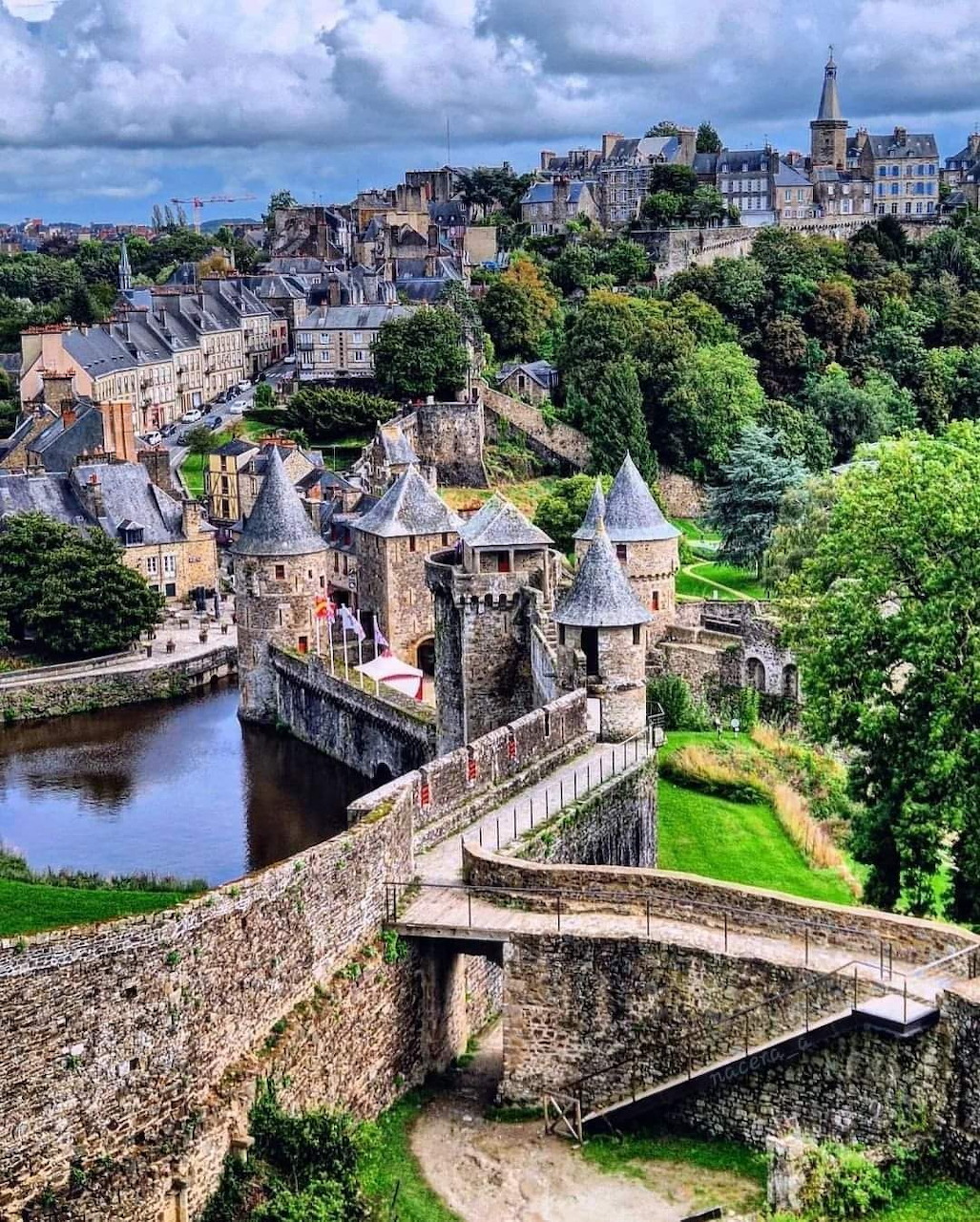 Aerial view of medieval castle with stone bridge, towers, and surrounding historic town beneath cloudy sky