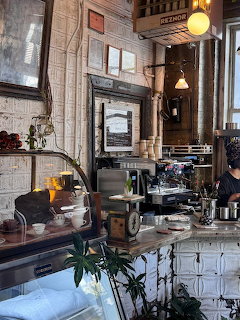 Cozy coffee shop interior with espresso machine, counter, framed wall decor, and hanging lights