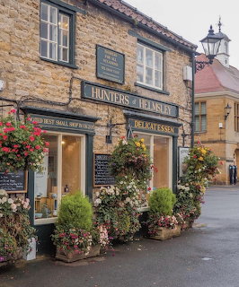 Hunters of Helmsley delicatessen shop with stone facade and colourful flower displays on a cobbled street