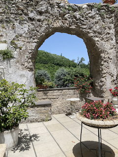 Old stone archway on a terrace with potted flowers and greenery under a blue sky