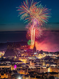 Colorful fireworks exploding above Edinburgh Castle and city buildings at night