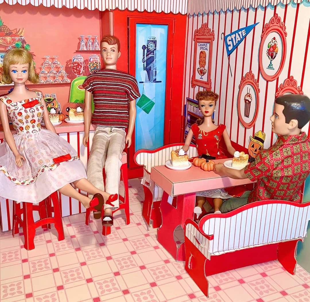 Vintage dollhouse kitchen with dolls around a pink table in a retro red and white room