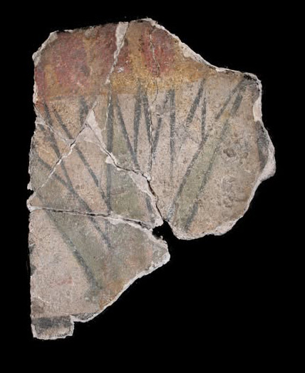 Fragmented ancient Egyptian plaster piece with faded painted lotus flower design on black background