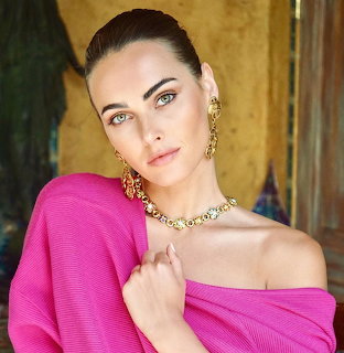 Woman in magenta off-shoulder top with gold earrings and necklace posing indoors